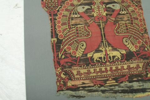 A samitum textile in blue red and yellow, mostly read peackock face each other above an Arabic script.