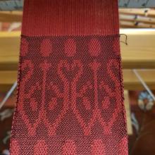 A red warp woven with a purple weft that creates the bacground with dots and a ivy/tree motif
