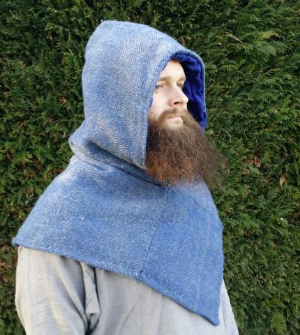 A man with a beard wearing a hood with a v hemline the hood is made of handwoven point twill in grey and blue