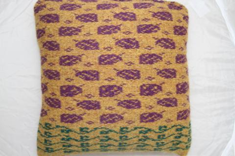 A pillow made of weft faced woven cloth in a yellow background rows of green ivy then rows of purple frett leaves