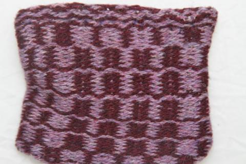 A weft faced woven small bag with a checkered pattern in light and dark purple.