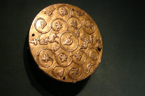 a decorative round piece of silver with a filagree design and threen holes one on each side and one on the bottom, possibly for attaching to cloth.
