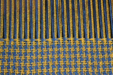 A hounds tooth cloth on the loom in yellow and blue