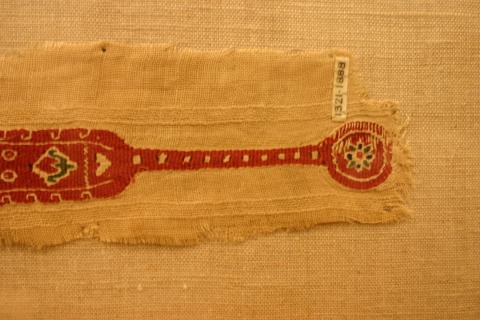 A tapestry woven band with a rose background the band narrows then widens back out to a circle.