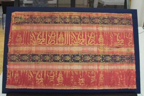 Red, blue and yellow silk textile with geometric designs and an Arabic script trasnlated as Glory to our lord the sultan"