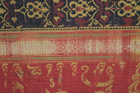 Red, blue and yellow silk textile with geometric designs and an Arabic script trasnlated as Glory to our lord the sultan"